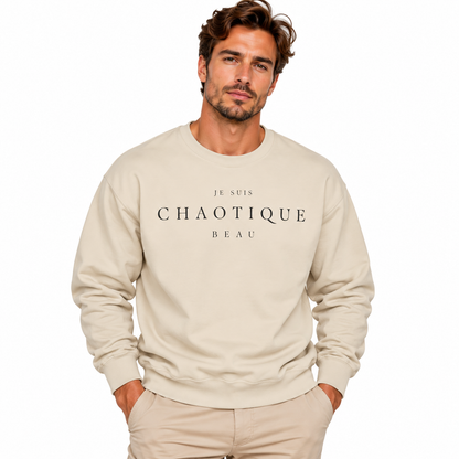 A man wearing a beige crewneck sweatshirt with the text 'JE SUIS CHAOTIQUE BEAU' printed in white across the chest, paired with beige pants, set against a plain white background.