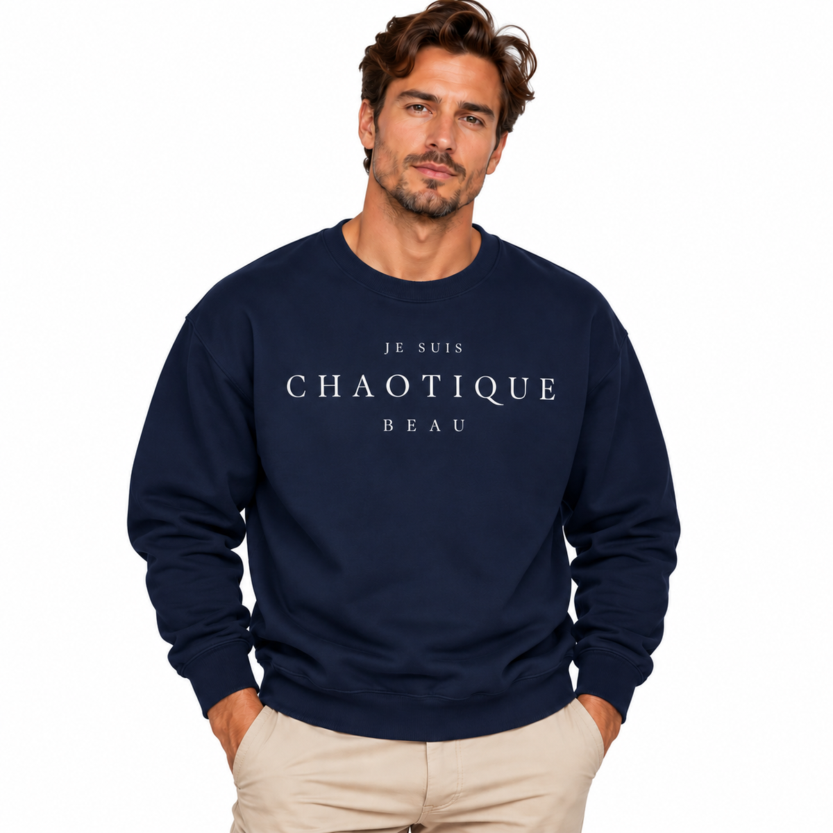 A man wearing a navy blue crewneck sweatshirt with the text 'JE SUIS CHAOTIQUE BEAU' printed in white across the chest, paired with beige pants, set against a plain white background.