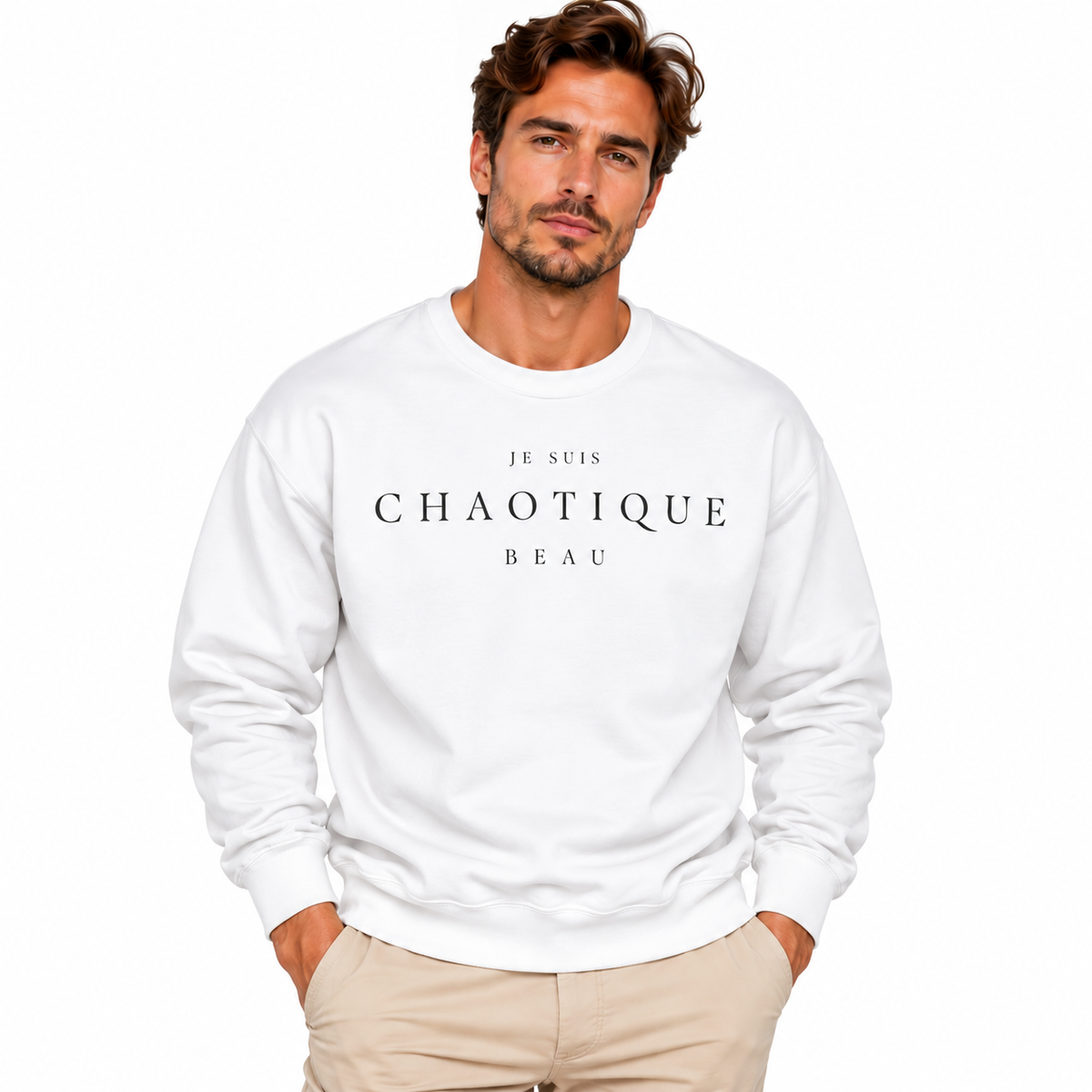 A man wearing a white crewneck sweatshirt with the text 'JE SUIS CHAOTIQUE BEAU' printed in white across the chest, paired with beige pants, set against a plain white background.