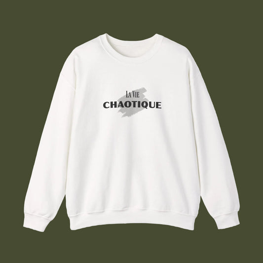 A white crewneck sweatshirt with a black graphic print on the chest reading 'LA VIE CHAOTIQUE' over a gray paint splatter design, displayed on a clean white background.