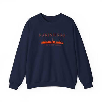 A navy crewneck sweatshirt with a bright orange “PARISIENNE” graphic, Paris skyline design, and “CHIC À MA FAÇON” text on the chest, displayed against a clean white background

