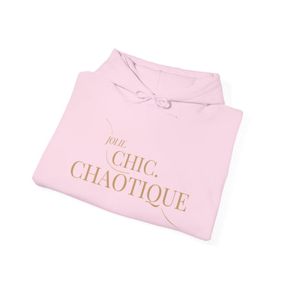 A folded light pink hoodie with a gold foil print reading 'Jolie CHIC. CHAOTIQUE' on a clean white background.