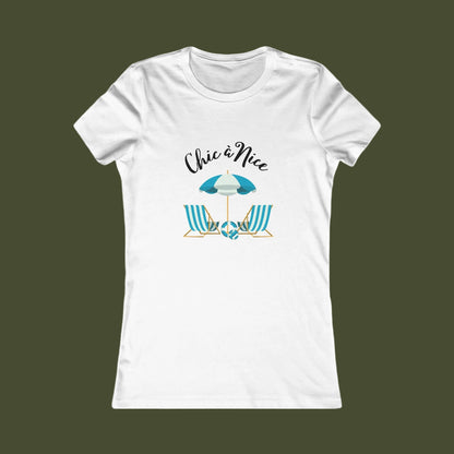 A white short-sleeve crewneck t-shirt with a graphic on the front showing a beach umbrella and two striped beach chairs under the text 'Chic a Nice'.