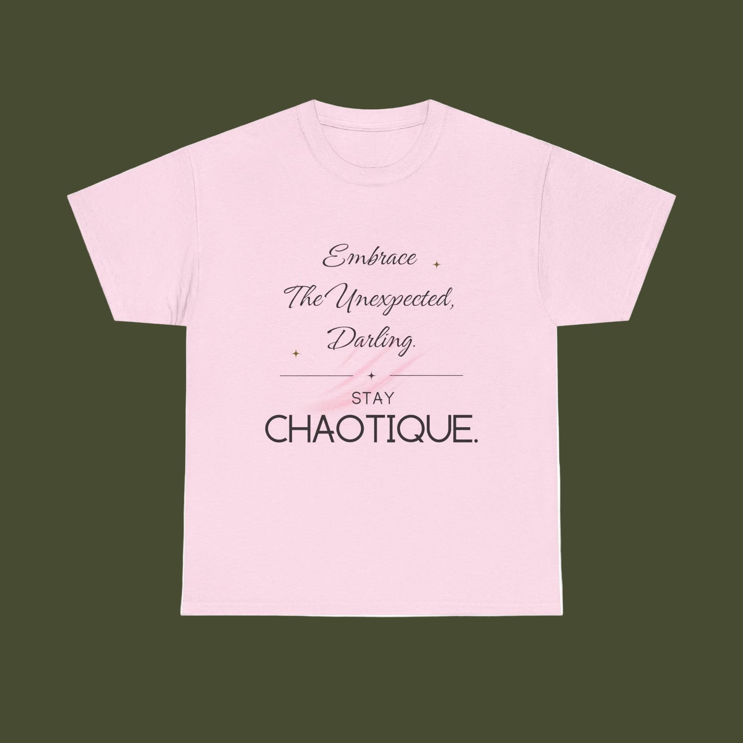 A light pink short-sleeve crewneck t-shirt with a typographic graphic on the front. The text reads 'Embrace The Unexpected, Darling' in a cursive font, followed by a horizontal line, 'STAY CHAOTIQUE.