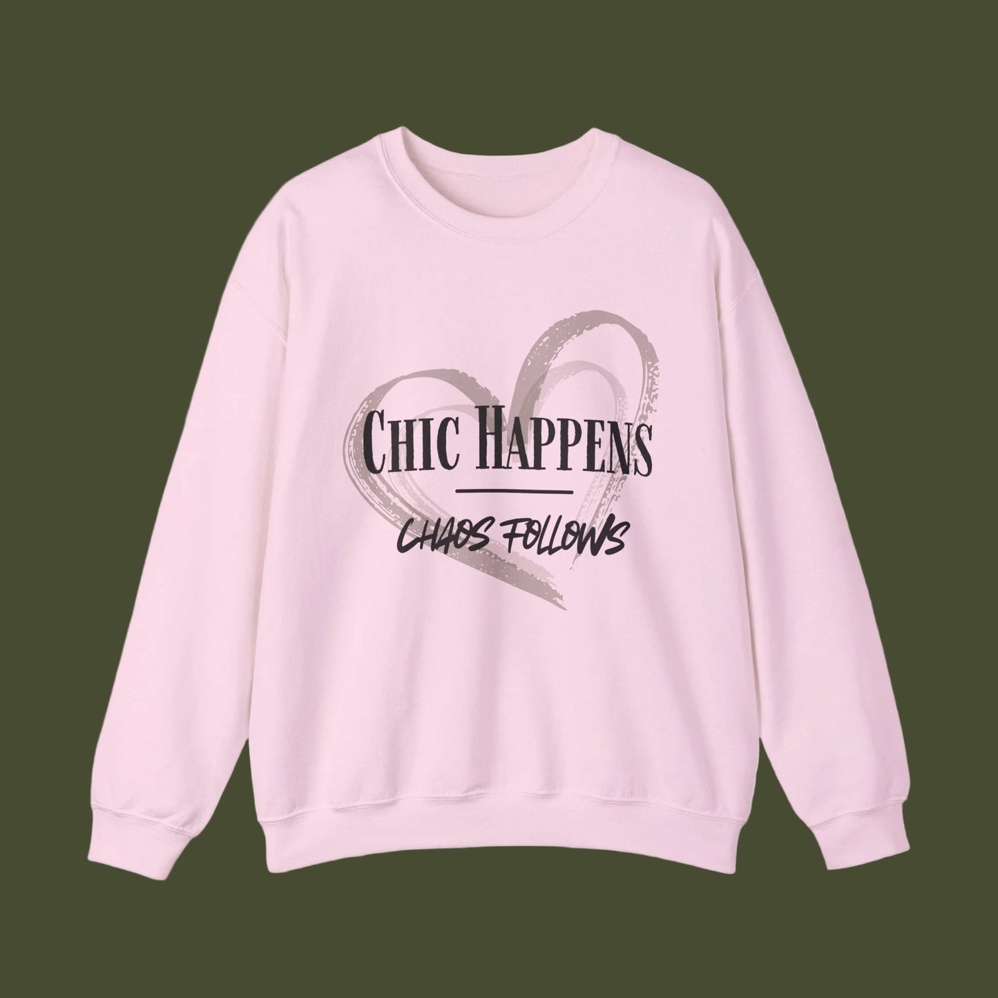 A light pink crewneck sweatshirt featuring a graphic print on the front with a gray brushstroke heart and the text 'CHIC HAPPENS' and 'CHAOS FOLLOWS' in black.