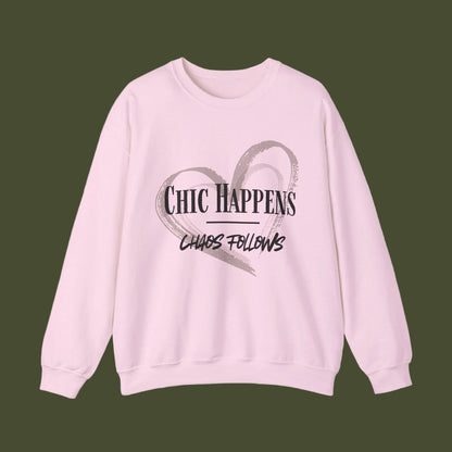 A light pink crewneck sweatshirt featuring a graphic print on the front with a gray brushstroke heart and the text 'CHIC HAPPENS' and 'CHAOS FOLLOWS' in black.