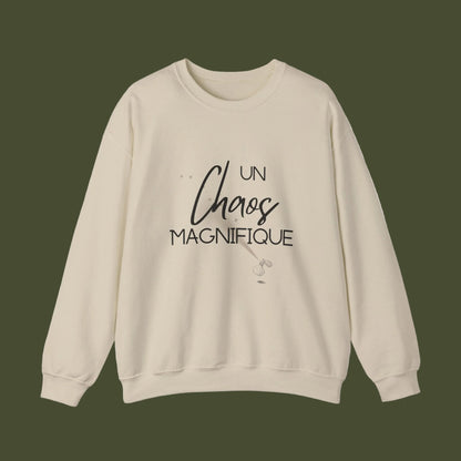 A beige crewneck sweatshirt with a black graphic text print reading 'UN Chaos MAGNIFIQUE' on the front, displayed against a plain white background.