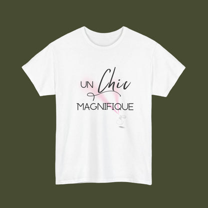 A white short-sleeve crewneck t-shirt featuring a French graphic print that reads 'UN Chic MAGNIFIQUE' in black script and block lettering, accented with a soft pink watercolor splash and a small white feather illustration.