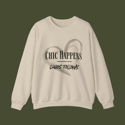 A beige crewneck sweatshirt with a black graphic print on the front featuring a heart outline and the text 'CHIC HAPPENS' and 'CHAOS FOLLOWS'.