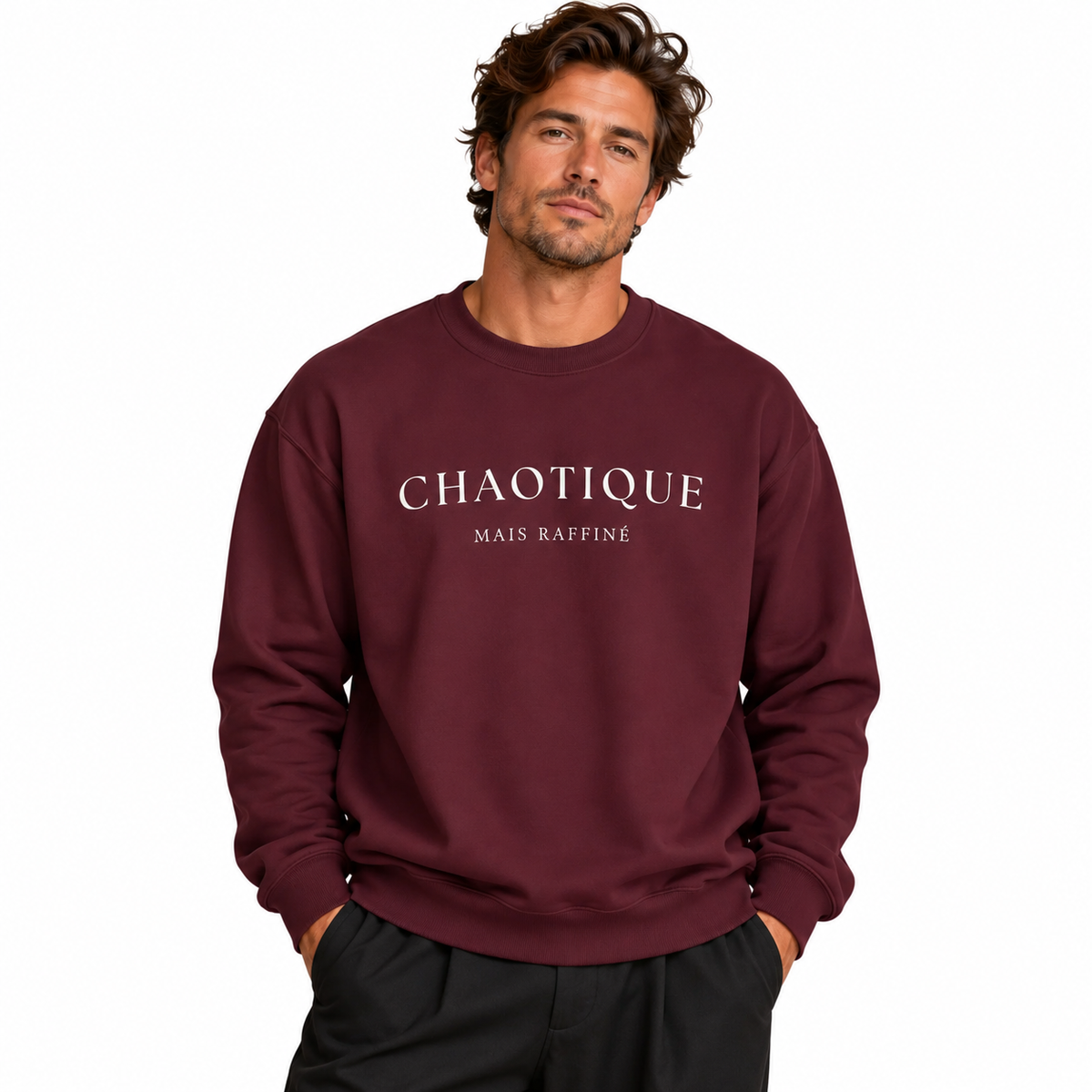 A man wearing a burgundy crewneck sweatshirt with 'CHAOTIQUE MAIS RAFFINÉ' printed in white across the chest, paired with black pants, set against a plain white background.