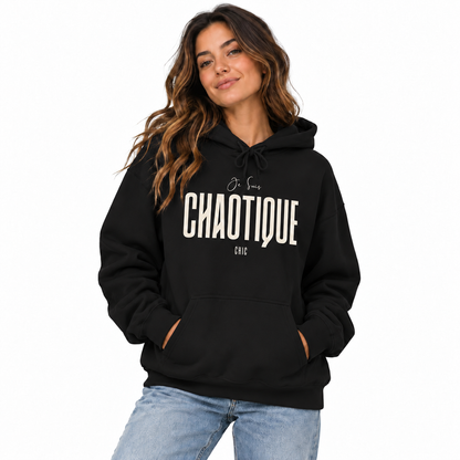 Woman wearing a black Je Suis CHAOTIQUE CHIC graphic hoodie with cream lettering and light blue jeans on a white studio background.