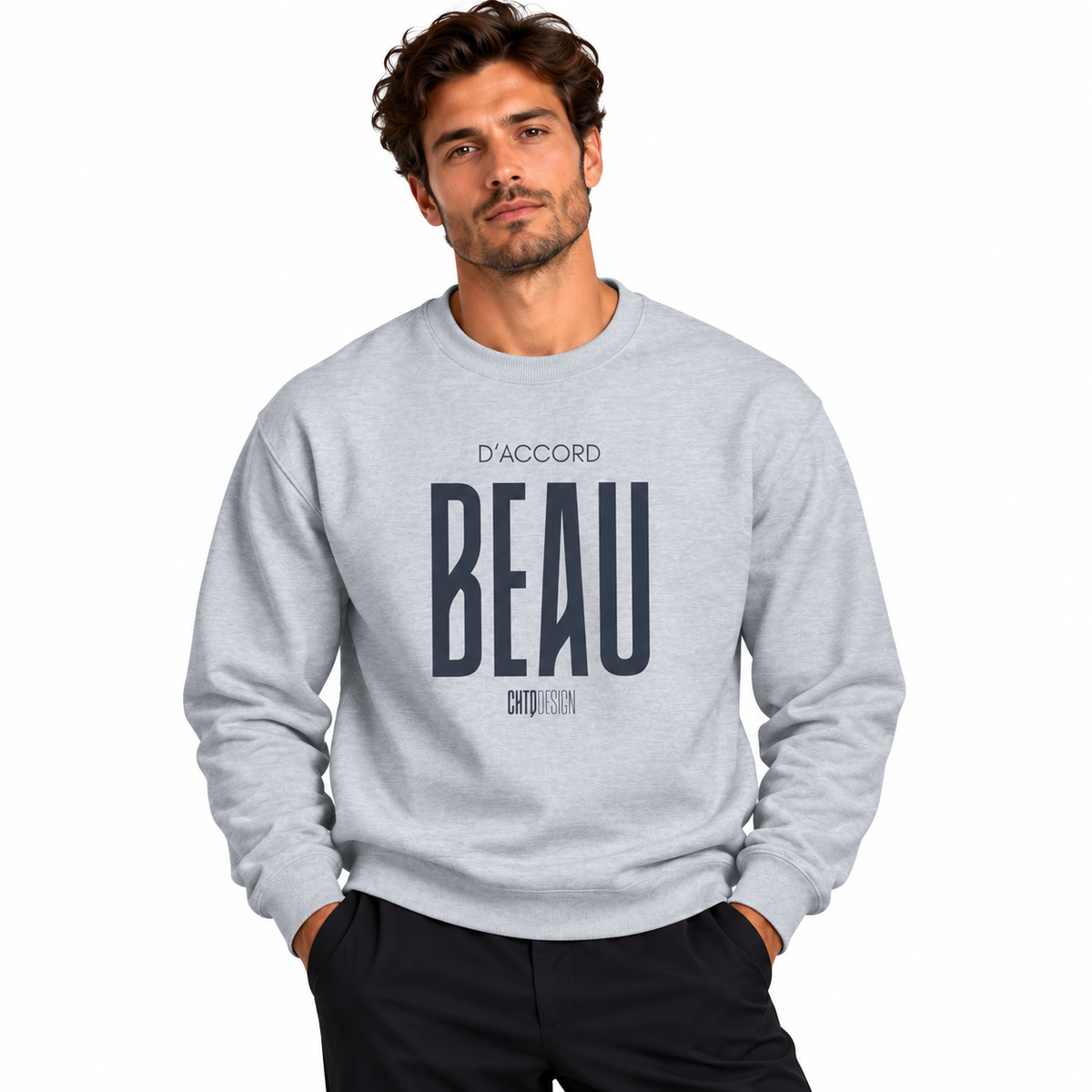 Male model wearing a light heather grey D’Accord BEAU graphic crewneck sweatshirt with black trousers against a white studio background.