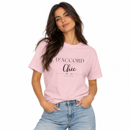 A woman modeling a light pink crewneck t-shirt with black printed text reading 'D'ACCORD Chic' on the front, paired with light-wash blue jeans against a plain white background.