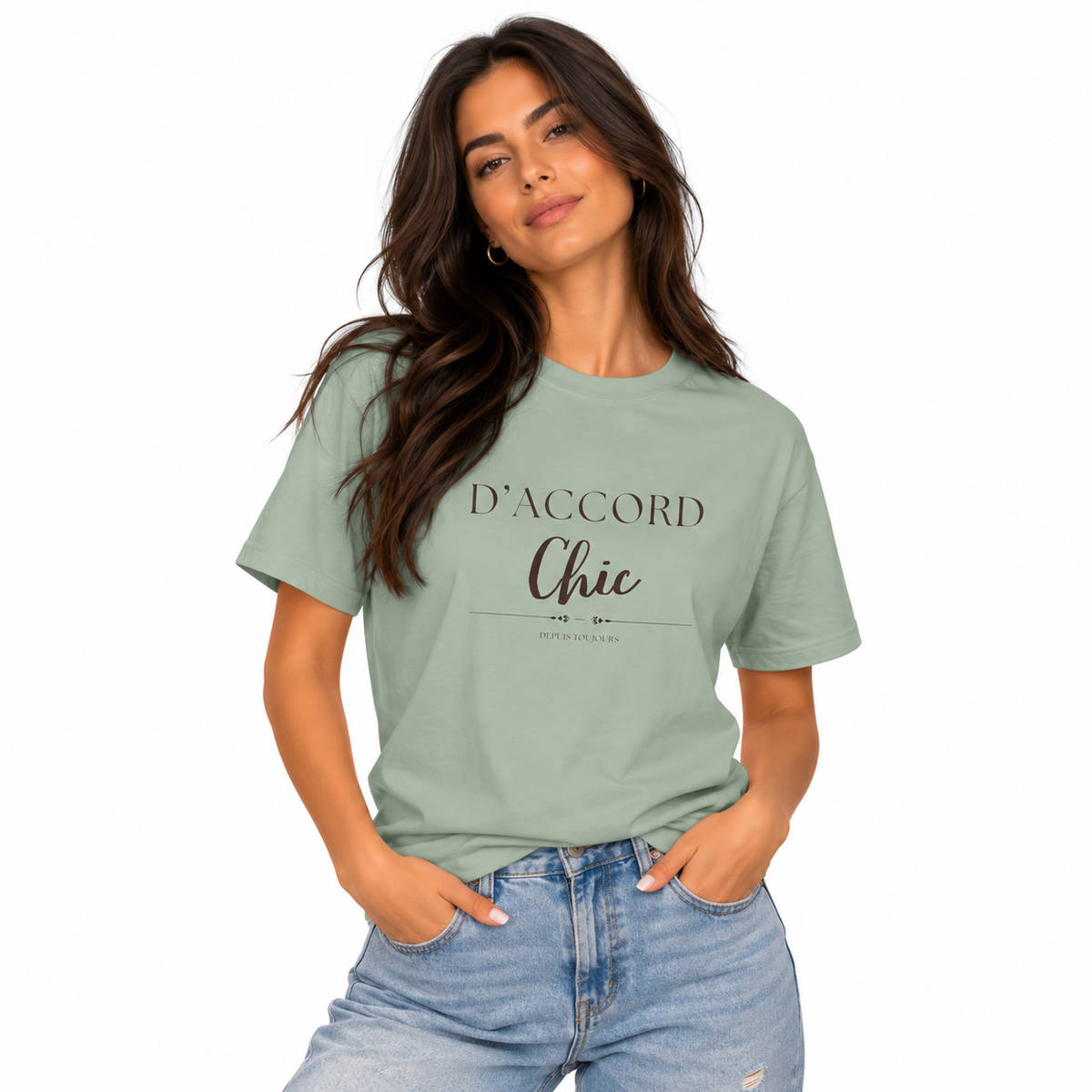 A woman modeling a sage green graphic t-shirt with the text 'D'ACCORD Chic' printed on the front, paired with light-wash blue jeans against a plain white background.