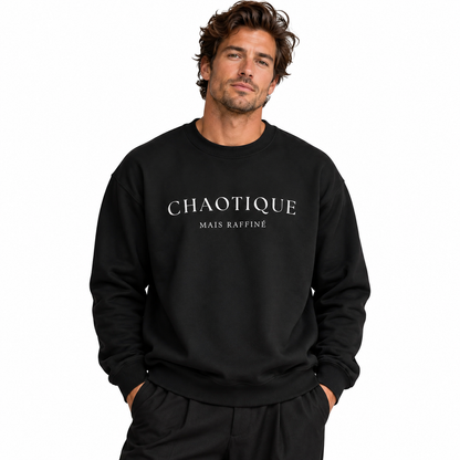 A man wearing a black crewneck sweatshirt with 'CHAOTIQUE MAIS RAFFINÉ' printed in white serif text across the chest, set against a plain white background.