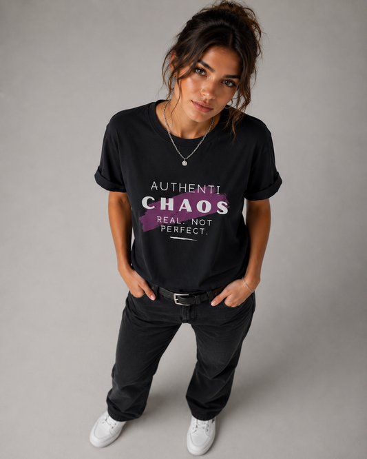 Woman wearing a black AuthentiChaos graphic T-shirt with white and purple typography in a modern gray studio setting.