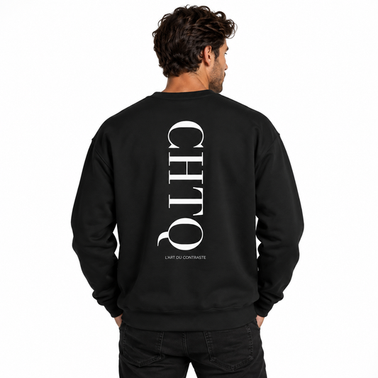 A man modeling a black crewneck sweatshirt from the back with a vertical white CHTQ graphic and “L’ART DU CONTRASTE” text, against a white studio background.