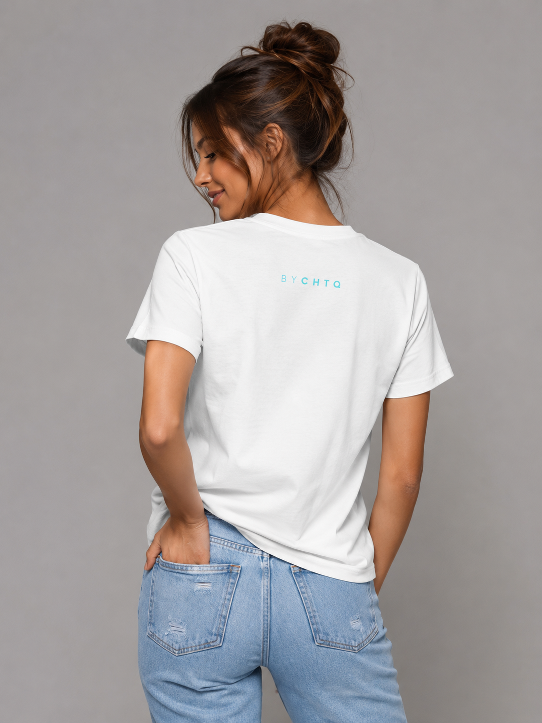 A woman wearing a white short-sleeve T-shirt shown from the back, featuring a small light blue 'BY CHTQ' detail below the neckline, paired with light-wash jeans against a neutral gray studio background.