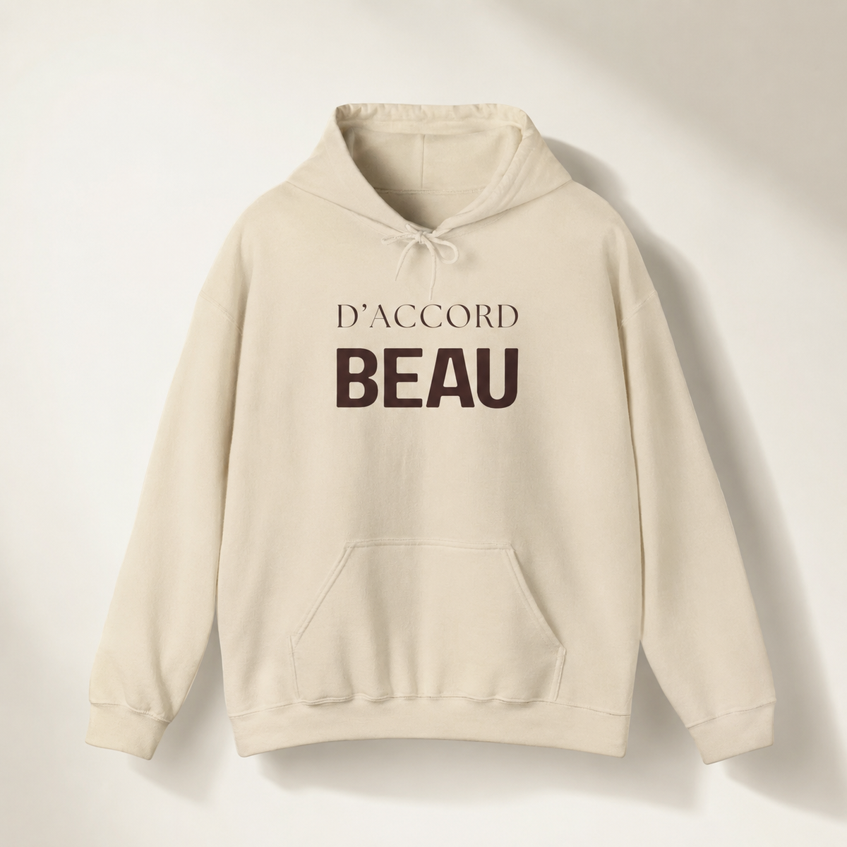 Beige D’Accord Beau pullover hoodie featuring dark brown typography on the front, displayed against a white studio background.