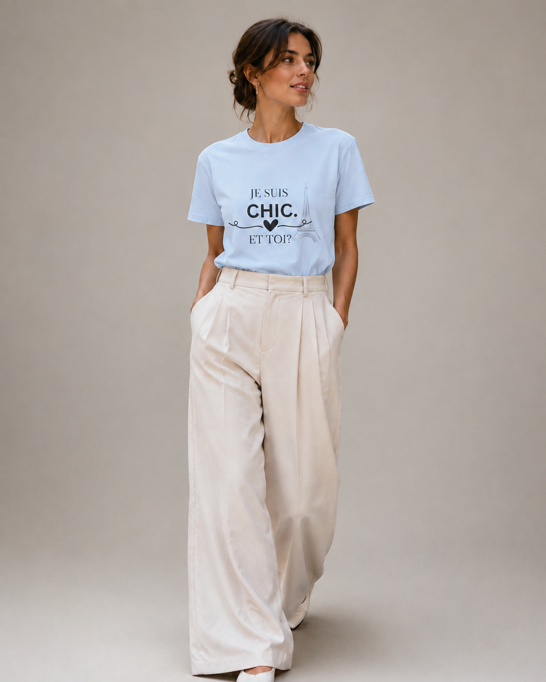 Woman wearing a light blue “Je Suis Chic. Et Toi?” graphic T-shirt with cream wide-leg trousers, photographed in a minimalist studio setting.
