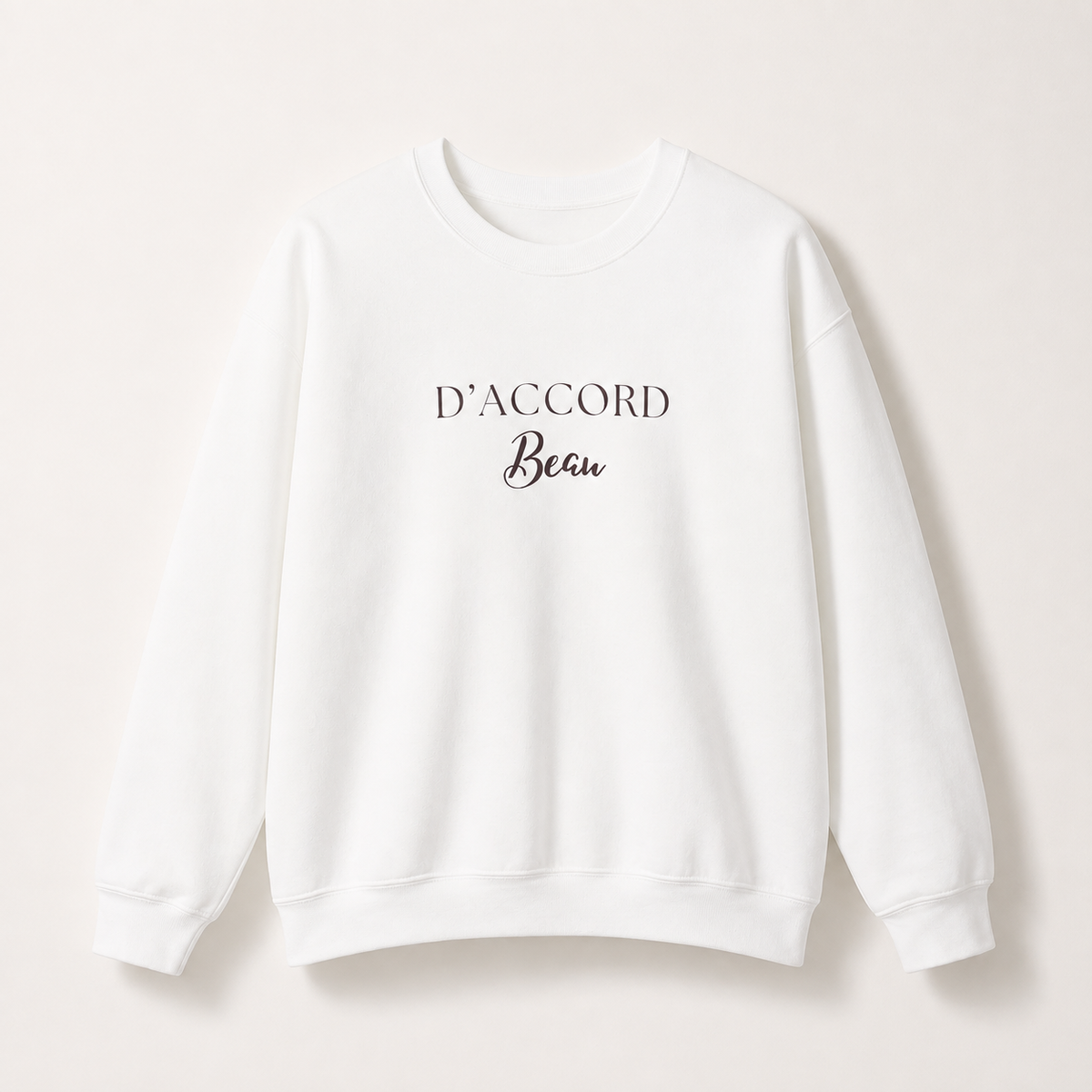 White D’Accord Beau crewneck sweatshirt featuring dark brown typography on the front, displayed against a light studio background.