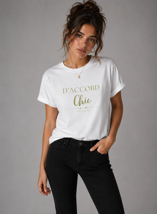 Woman wearing a white D’Accord Chic graphic T-shirt with olive-gold typography and black jeans in a gray studio setting.