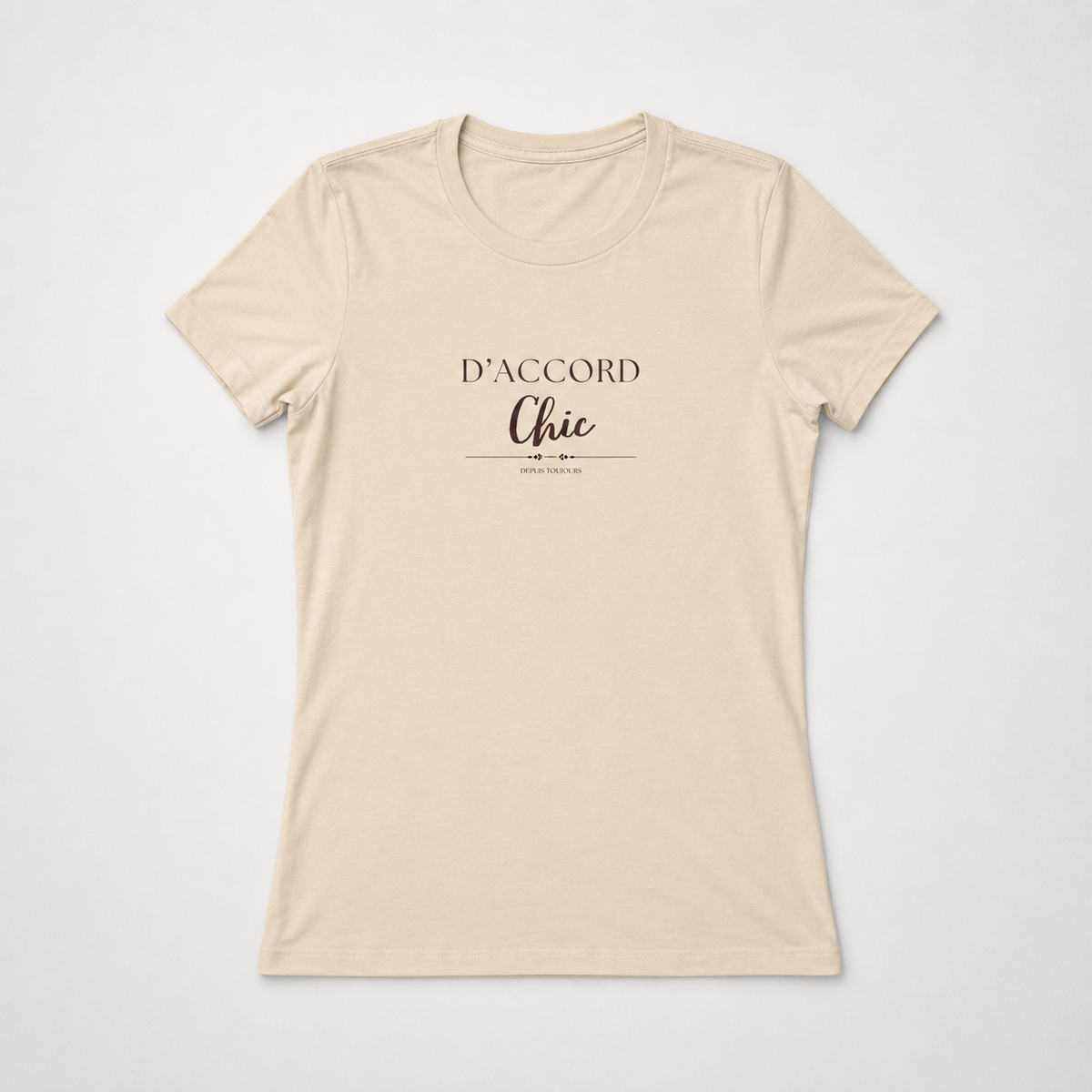 Beige short-sleeve crewneck T-shirt featuring the “D’Accord Chic” graphic in black and brown lettering on the front, displayed against a light gray background.