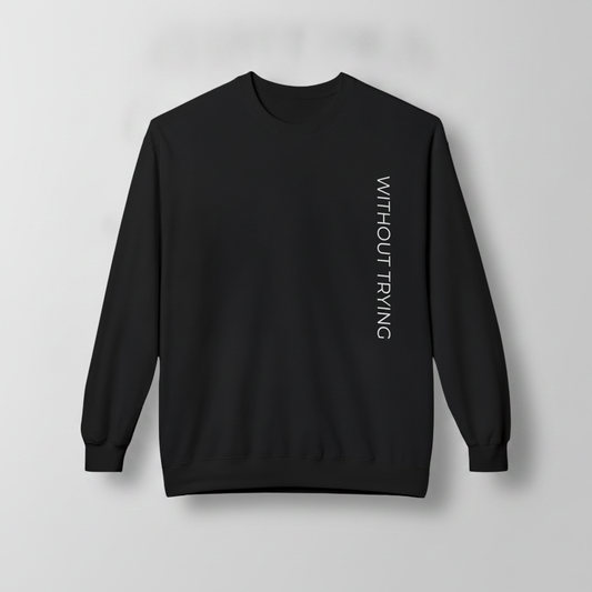 Black crewneck sweatshirt featuring a vertical white “WITHOUT TRYING” graphic on the front, displayed against a light gray background.