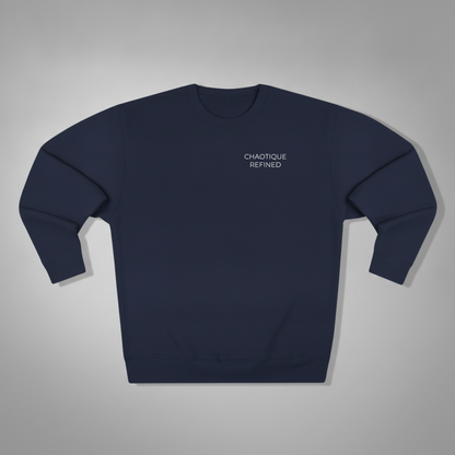 A navy blue crewneck sweatshirt with 'CHAOTIQUE REFINED' printed in white text on the left chest, displayed flat against a neutral gray background.