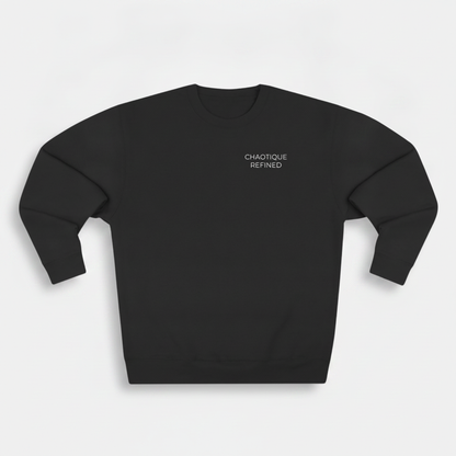 A black crewneck sweatshirt with the words 'CHAOTIQUE REFINED' printed in small white text on the left chest, displayed on a light gray background.