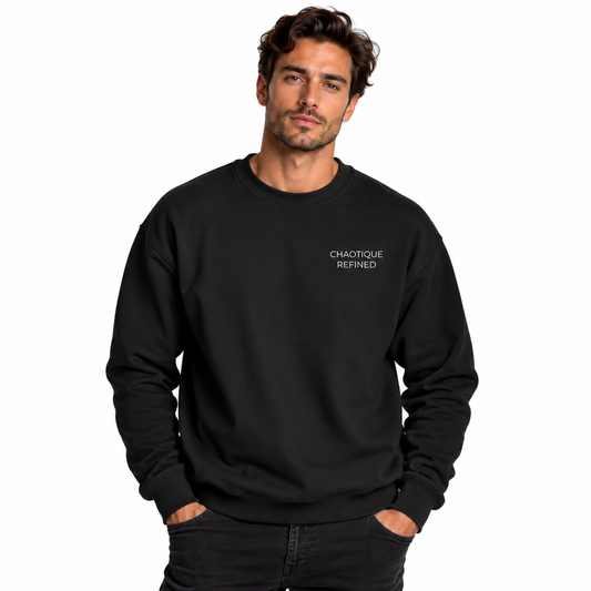 A man wearing a black crewneck sweatshirt with “CHAOTIQUE REFINED” printed in white text on the left chest, against a plain white studio background.