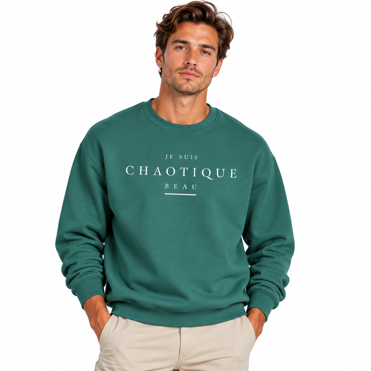 A man wearing a navy blue crewneck sweatshirt with white printed text reading 'JE SUIS CHAOTIQUE BEAU' on the chest, paired with light beige pants, against a plain white background.
