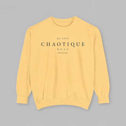 A pale yellow crewneck sweatshirt with the French text 'JE SUIS CHAOTIQUE BEAU' printed in black on the chest, displayed flat against a solid gray background.