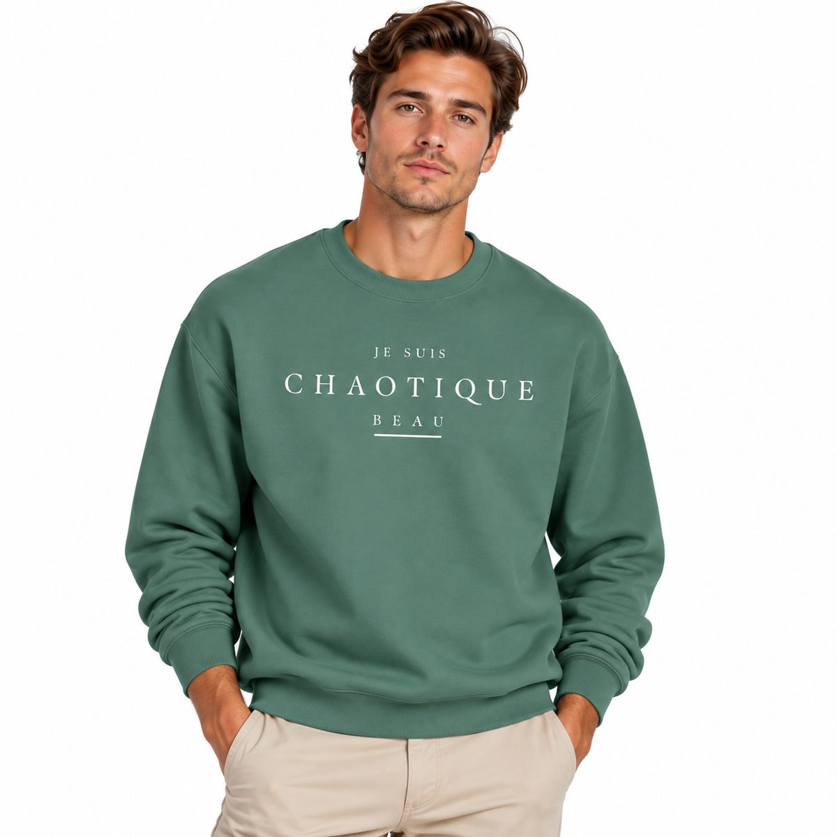 A man wearing a green crewneck sweatshirt with white text reading 'JE SUIS CHAOTIQUE BEAU' on the chest, paired with light beige pants, against a plain white background.