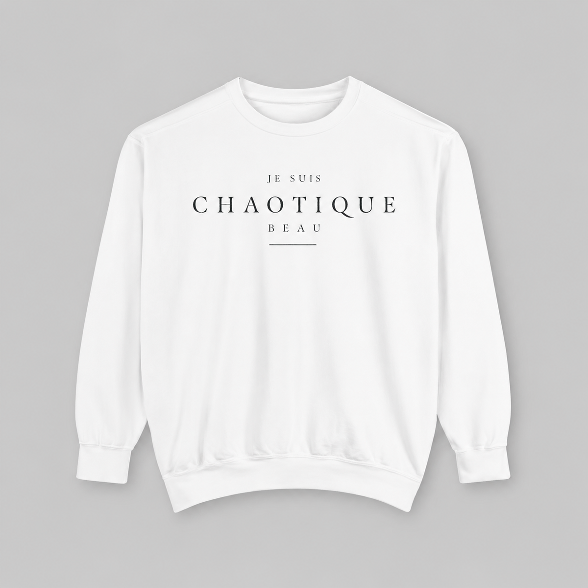 A white crewneck sweatshirt with black printed text reading 'JE SUIS CHAOTIQUE BEAU' on the chest, displayed flat against a solid gray background.