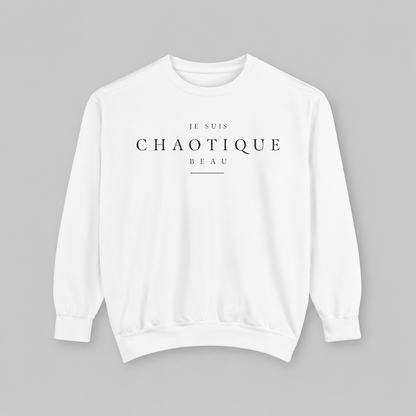 A white crewneck sweatshirt with black printed text reading 'JE SUIS CHAOTIQUE BEAU' on the chest, displayed flat against a solid gray background.