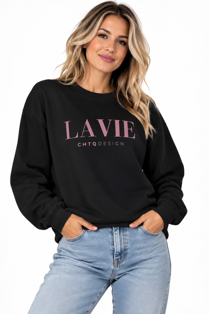A woman wearing a maroon crewneck sweatshirt with 'LAVIE CHTQDESIGN' printed in light pink across the chest, paired with light blue jeans, against a plain white background.