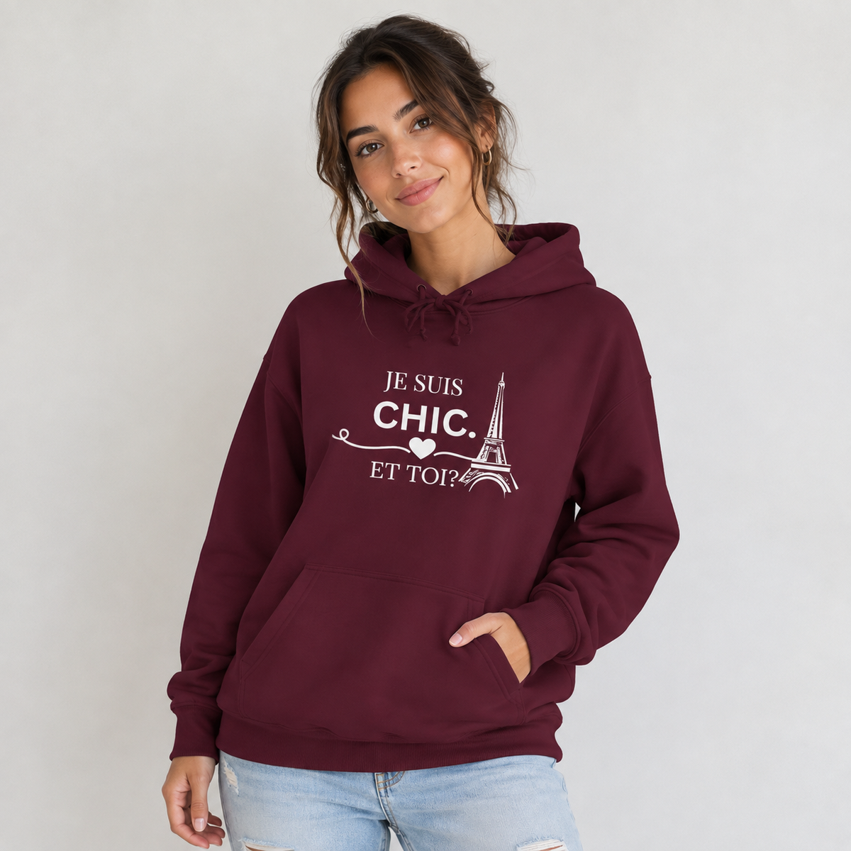 A woman wearing a maroon pullover hoodie with a white graphic print that reads 'JE SUIS CHIC. ET TOI?'.