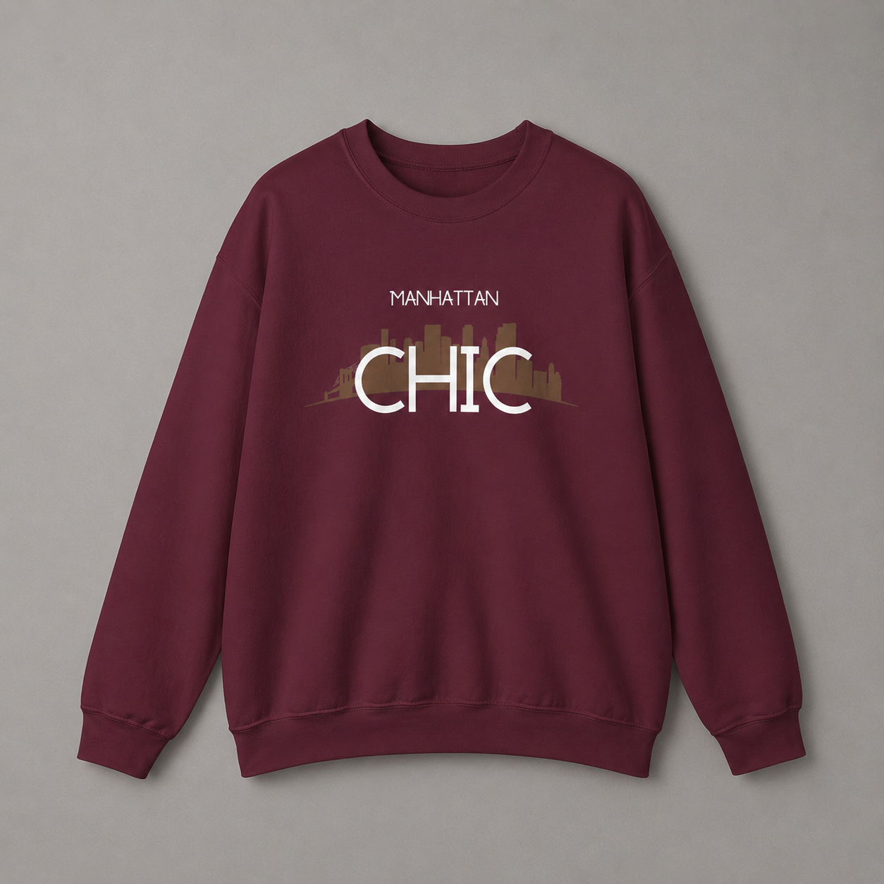 Maroon MANHATTAN CHIC crewneck sweatshirt featuring black typography and a muted olive New York skyline graphic, 
 against a neutral gray studio background.