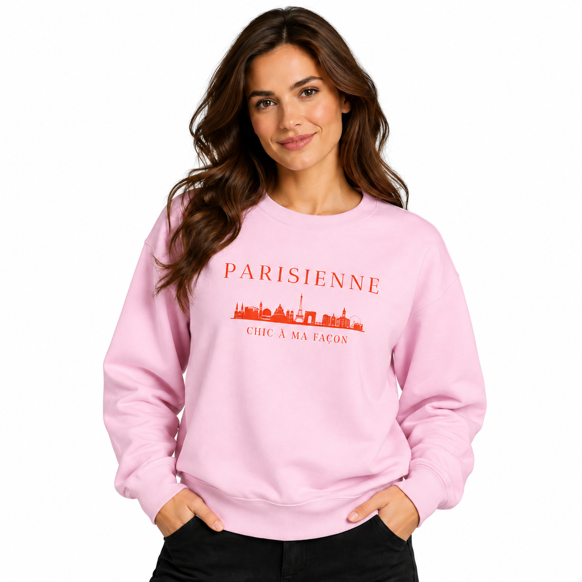 A woman modeling a light pink crewneck sweatshirt with a red graphic print that reads 'PARISIENNE' and 'CHIC A MA FACON' with a skyline illustration, set against a plain white background.
