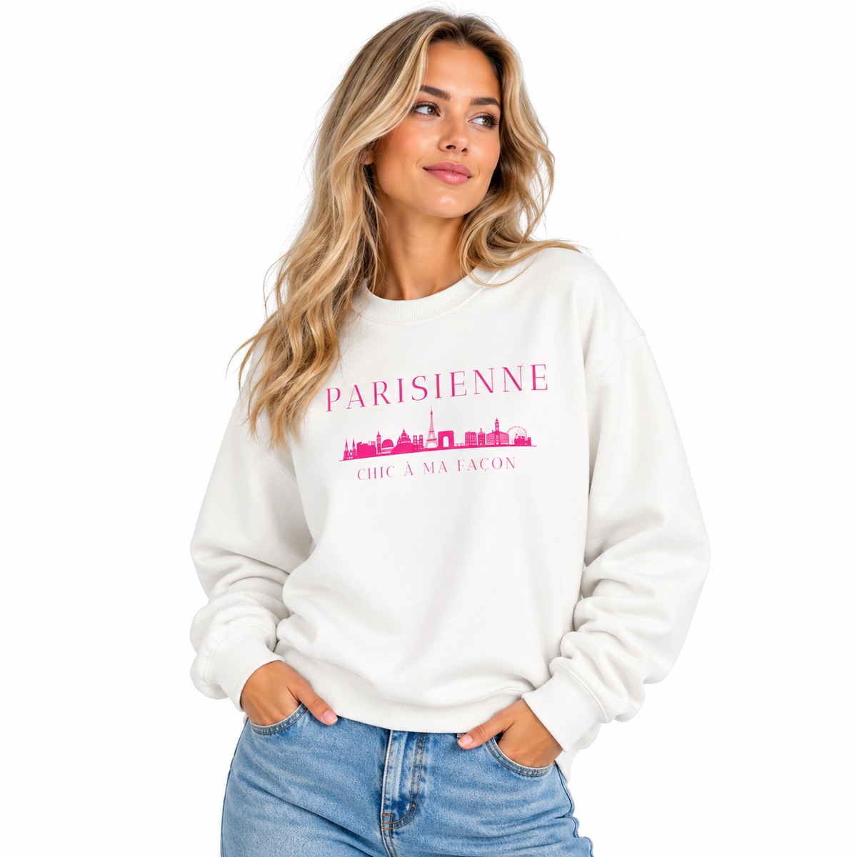 A woman wearing a cream-colored crewneck sweatshirt with a pink graphic that reads 'PARISIENNE' and 'CHIC A FACON' with a skyline illustration, paired with blue jeans against a plain white background.