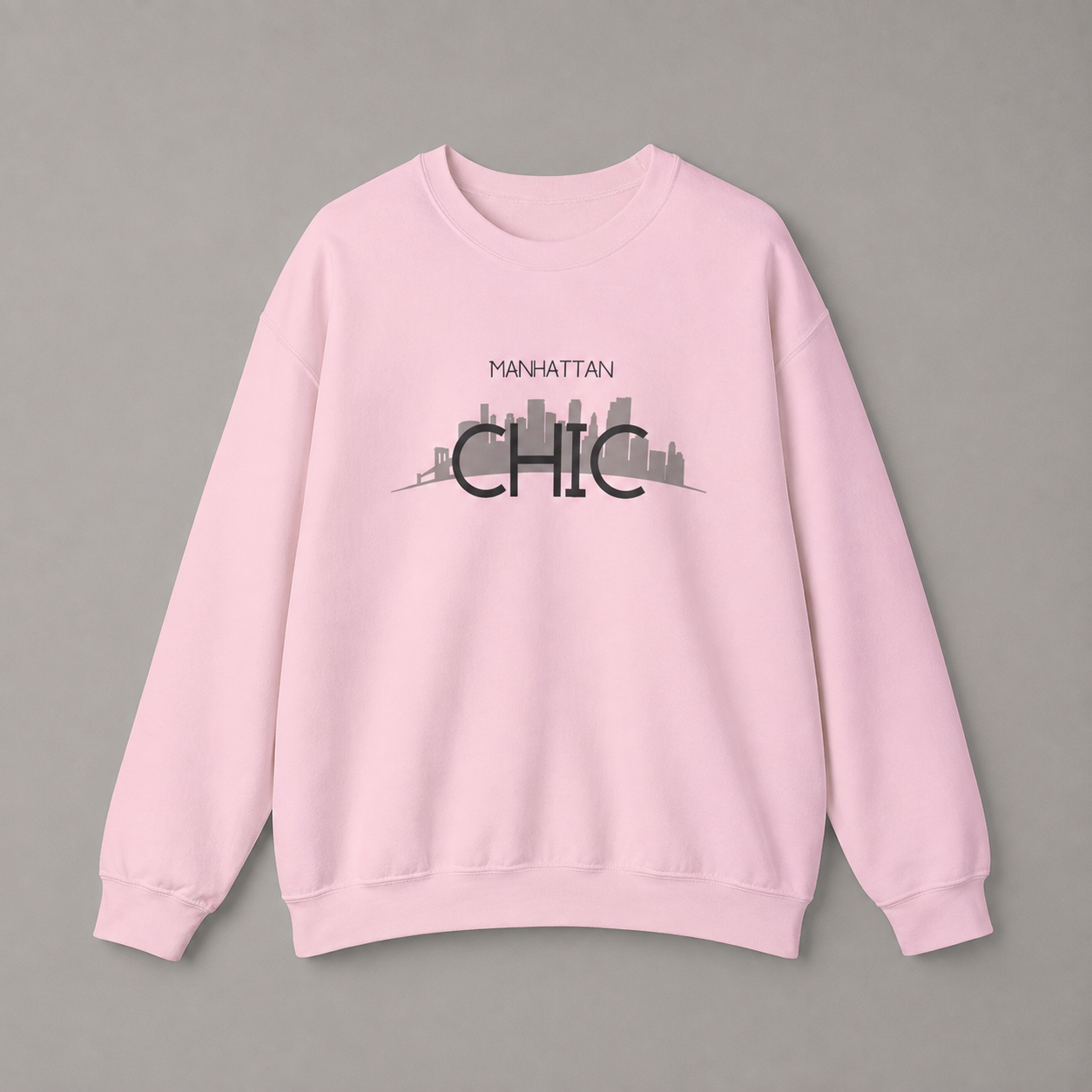 Light pink MANHATTAN CHIC crewneck sweatshirt featuring black typography and a muted olive New York skyline graphic, 
 against a neutral gray studio background.