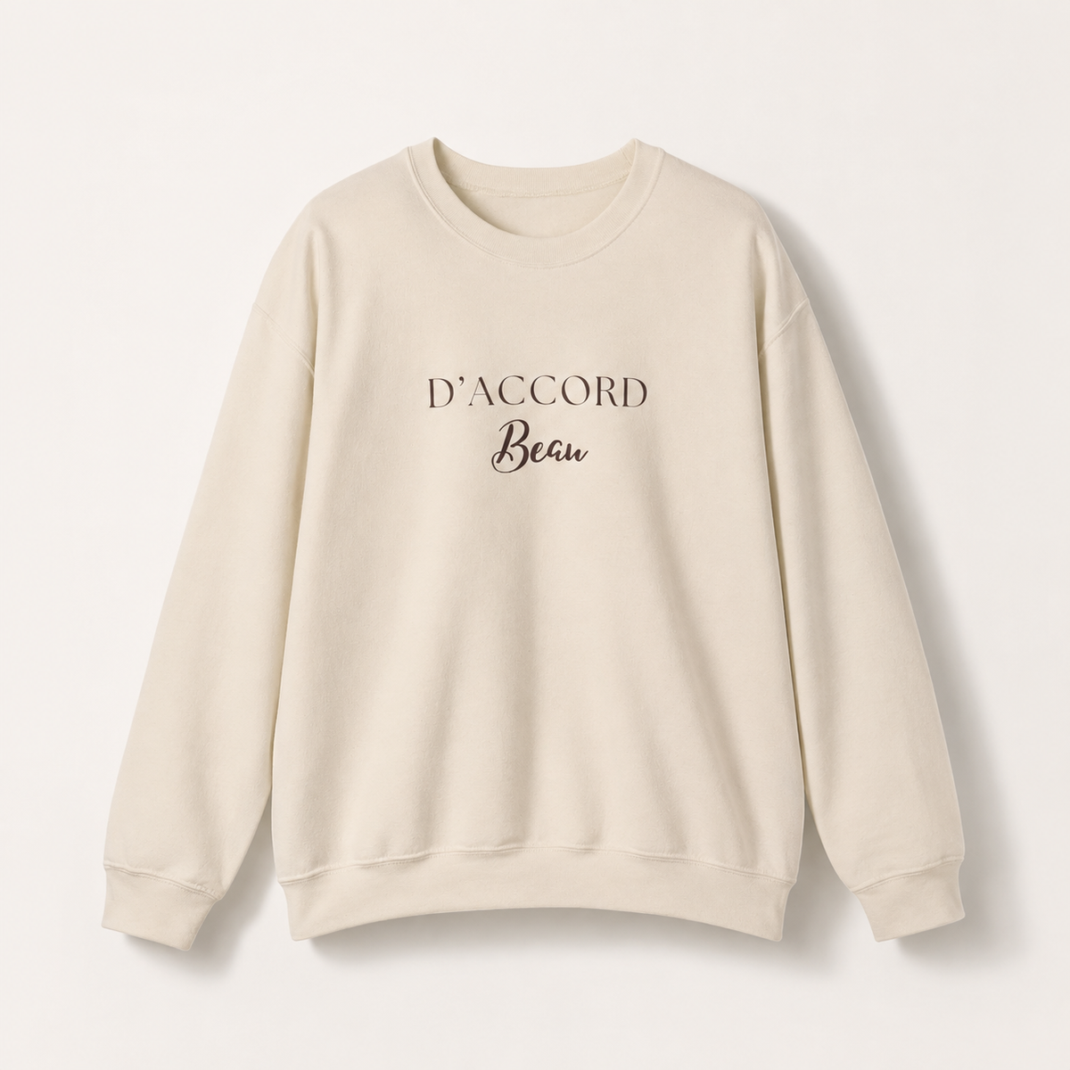 Beige D’Accord Beau crewneck sweatshirt featuring dark brown typography on the front, displayed against a light studio background.