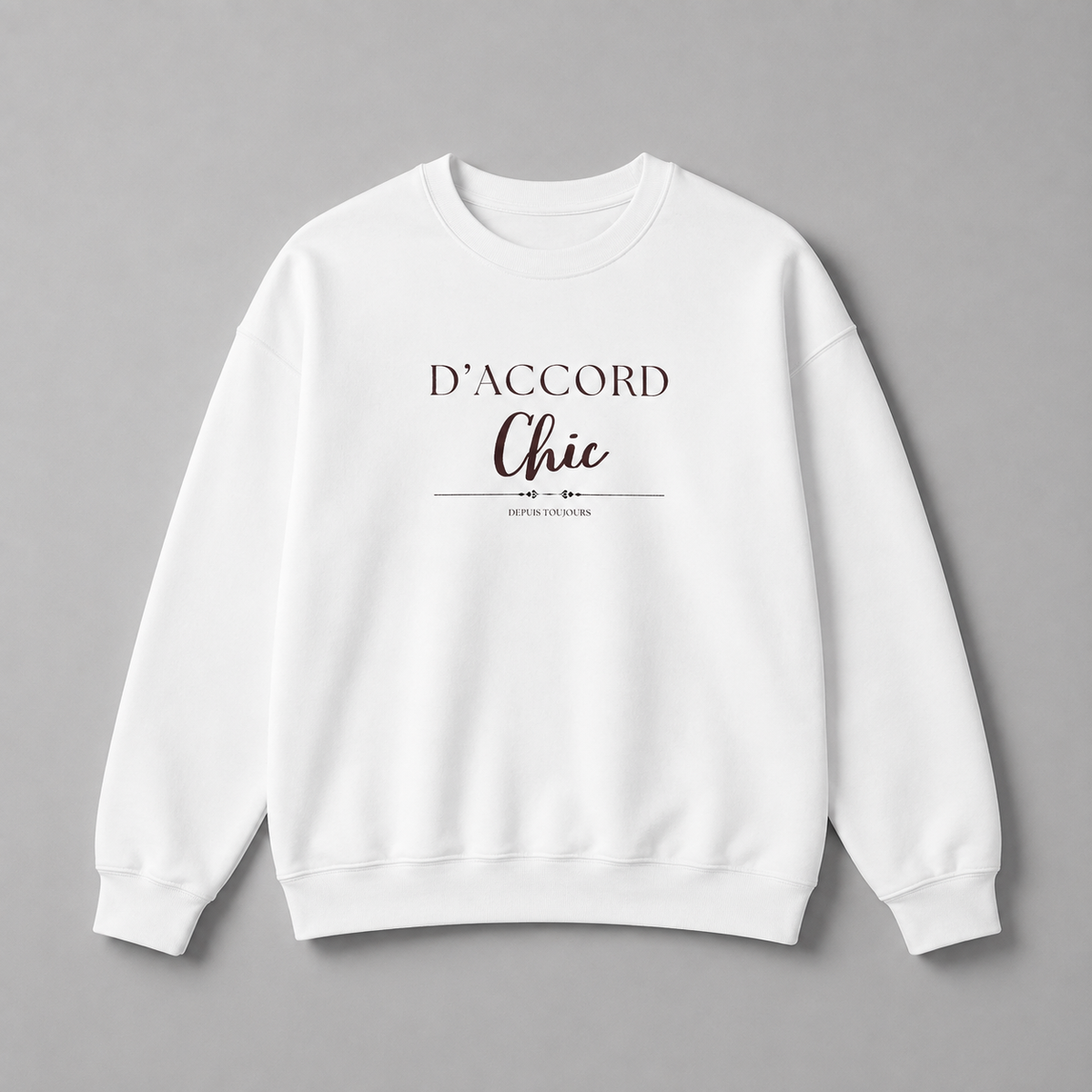 White D’Accord Chic crewneck sweatshirt with dark brown chest typography, displayed flat against a neutral grey studio background.